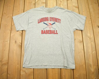 Könnte beinhalten: Graues T-Shirt mit einem roten und blauen Baseball-Logo, auf dem "Lansing Everett Baseball" steht.