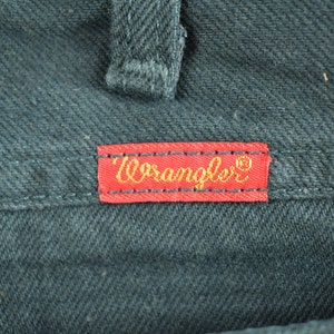 Op de afbeelding: Een rood leren label met gouden stiksels en het woord "Wrangler" in gouden letters.