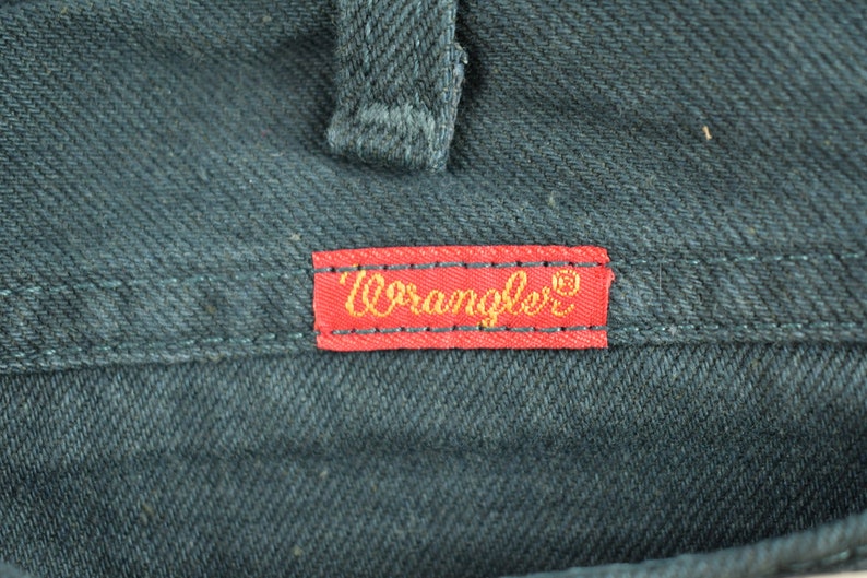 Op de afbeelding: Een rood leren label met gouden stiksels en het woord "Wrangler" in gouden letters.