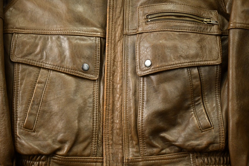 May include: A brown leather jacket with two large flap pockets and a zippered pocket on the chest.