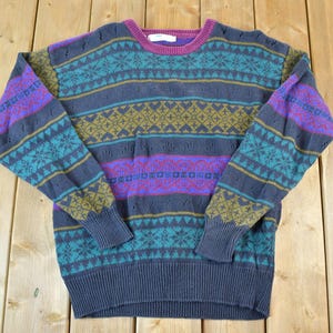 Peut inclure: Un pull rayé multicolore avec un motif géométrique. Le pull est en tissu tricoté doux et présente un col rond.