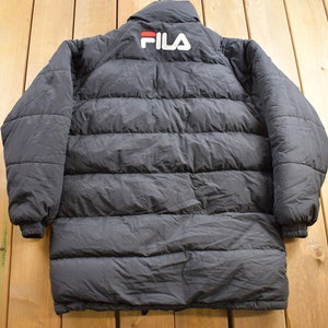 May include: Black puffer jacket with a FILA logo on the back. The jacket has a zip fastening and a stand-up collar.