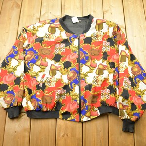 May include: A black bomber jacket with a colorful, patterned design featuring gold chains, red hats, and blue and red shoes.