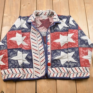 May include: A red, white, and blue cardigan with a star pattern. The cardigan has a button closure and a collar.