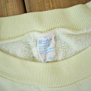 May include: A pale yellow sweatshirt with a blue and white care label that reads "60% cotton 40% acrylic 50% cotton 50% wool 50% polyester".
