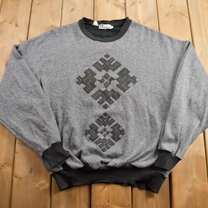 May include: A gray sweatshirt with a black geometric design on the front. The design is a repeating pattern of squares and triangles.