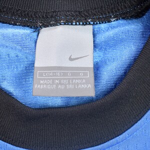 May include: A close-up of a blue and black Nike shirt tag with the text "LC14-16D G G MADE IN SRI LANKA FABRIQUE AU SRI LANKA".