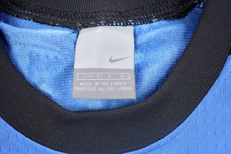 May include: A close-up of a blue and black Nike shirt tag with the text "LC14-16D G G MADE IN SRI LANKA FABRIQUE AU SRI LANKA".