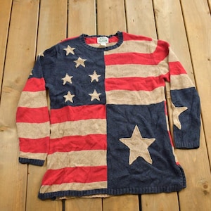 Könnte beinhalten: Ein blauer und roter Strickpullover mit einem weißen und roten amerikanischen Flaggenmuster. Der Pullover hat lange Ärmel und einen Rundhalsausschnitt.