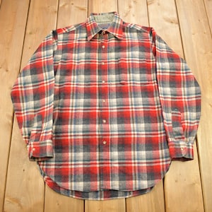 May include: A red, blue, and white plaid flannel shirt with long sleeves and a button-down front.