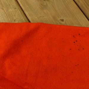 K&ouml;nnte beinhalten: Nahaufnahme eines leuchtend orangenen Stoffes mit ein paar kleinen dunkelbraunen Flecken.