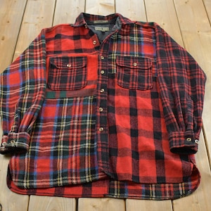 Peut inclure: Une chemise à manches longues boutonnée présentant un motif patchwork composé de divers tissus en flanelle à carreaux rouges, noirs et bleus. La chemise comprend un col classique, deux poches poitrine à rabat boutonné et des poignets boutonnés.