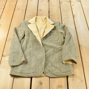 May include: A long-sleeved blazer featuring a textured green and brown micro-check pattern on the exterior, contrasted by a solid light tan lapel and interior lining, complete with two front patch pockets and a standard notched collar design.