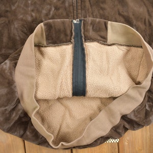 May include: A brown suede jacket with a zipper closure and a brown fleece lining.