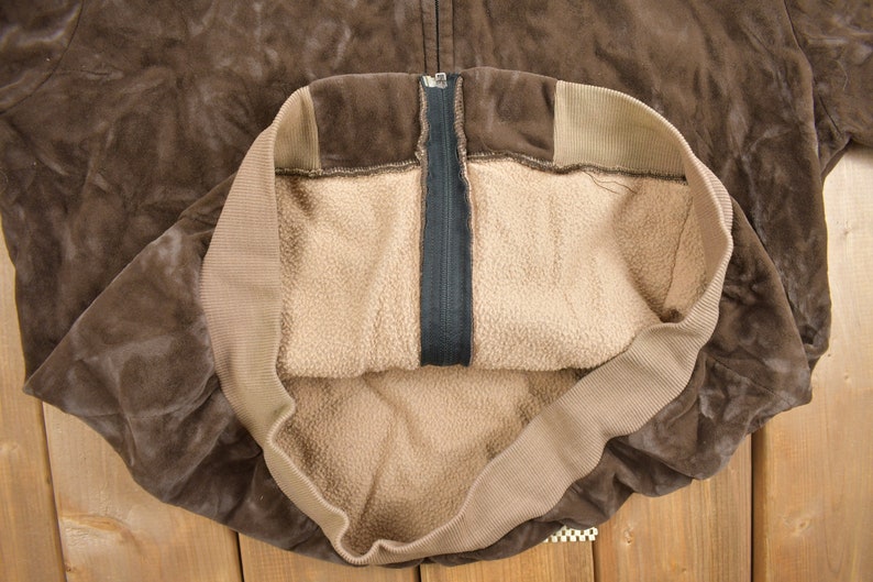 May include: A brown suede jacket with a zipper closure and a brown fleece lining.