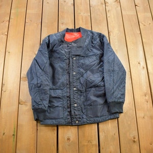 May include: A dark blue quilted jacket with a red lining and a button closure. The jacket has multiple pockets and a stand-up collar.