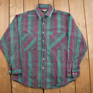May include: A long-sleeved plaid shirt with a button-down collar. The shirt is green and purple with a checkered pattern.