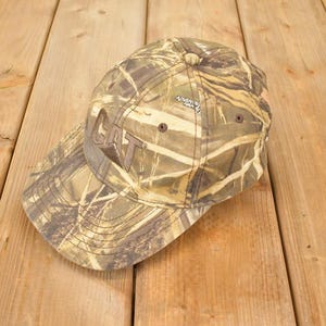 Könnte beinhalten: Tarnfarbene Baseballkappe mit dem Wort "CAT" auf der Vorderseite gestickt. Die Kappe hat einen gebogenen Schirm und einen verstellbaren Riemen. Der Hut ist aus strapazierfähigem Material gefertigt und für den Außenbereich konzipiert.