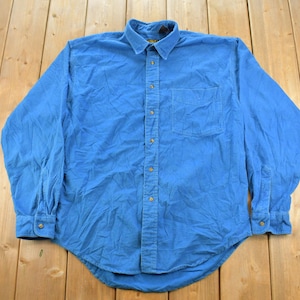 May include: A long-sleeved button-down shirt in a solid bright blue colour. The shirt features a standard collar, a single chest pocket on the left side, and a full-length front button placket with matching blue buttons on the cuffs and front.