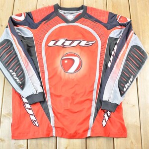 May include: Red, black, and gray long-sleeved paintball jersey with the word "dye" in white across the chest. The jersey has a V-neck and padded sections on the sleeves. The design includes a circular logo with a red and white design.