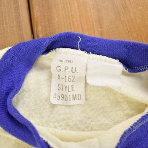 May include: A white t-shirt with a blue and white striped collar. The tag on the shirt reads "G.P.U. A-162 STYLE 45901 MO".