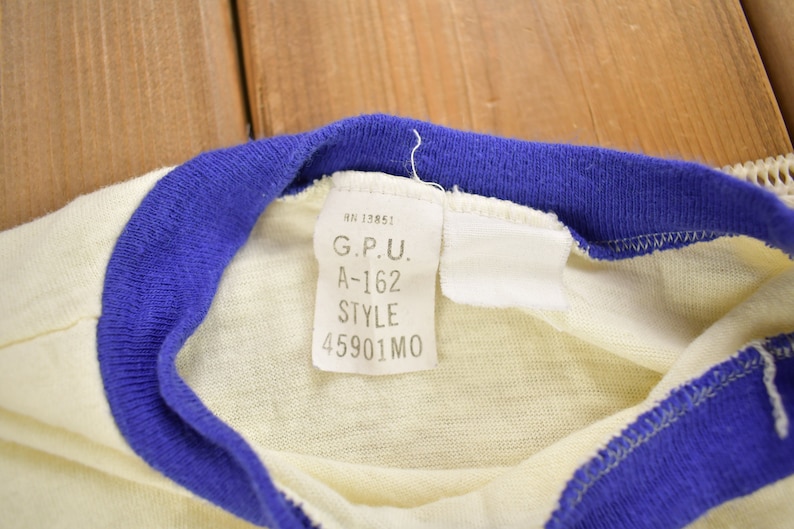 May include: A white t-shirt with a blue and white striped collar. The tag on the shirt reads "G.P.U. A-162 STYLE 45901 MO".