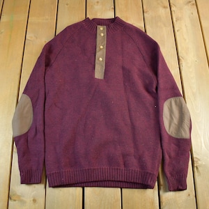 Puede incluir: Un su&eacute;ter burdeos con dobladillo y pu&ntilde;os acanalados. El su&eacute;ter presenta una tapeta abotonada, coderas y cuello redondo. Las coderas y la tapeta son de color marr&oacute;n claro. El su&eacute;ter est&aacute; hecho de un material suave y c&aacute;lido.