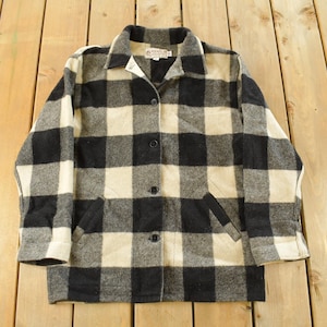 Può includere: Giacca a quadri neri, bianchi e grigi con collo e tre bottoni. La giacca ha due tasche anteriori e maniche lunghe. La giacca è realizzata in un materiale spesso e caldo.