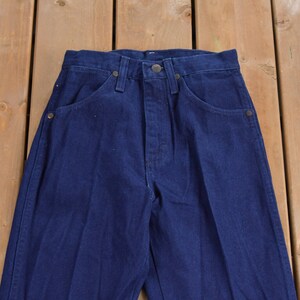 May include: A pair of dark blue denim jeans with a straight leg fit. The jeans have a classic five-pocket style and a button fly.