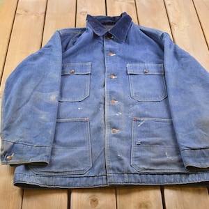 May include: A blue denim work jacket with a corduroy collar and multiple pockets. The jacket has a button-up front closure and appears to be vintage.