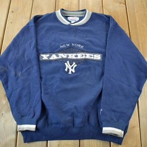 Può includere: Felpa blu navy girocollo con la scritta "NEW YORK YANKEES" in bianco e grigio, e il logo della squadra. La felpa ha polsini e finiture del colletto a righe grigie e bianche. L'indumento è realizzato in un materiale morbido e confortevole.