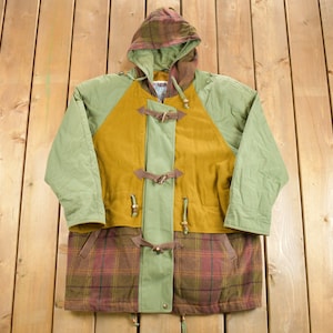 May include: A multi-coloured hooded jacket with a plaid pattern on the hood and lower section. The jacket features a mustard-coloured centre panel, olive green sleeves, and brown toggle closures. The jacket is made of a durable material.