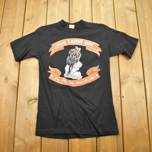 May include: Black t-shirt with a graphic of a biker riding a motorcycle. The graphic is surrounded by a banner that reads "HOG LABOR DAY AUG 30th, 31st, Sept 1st 1989".