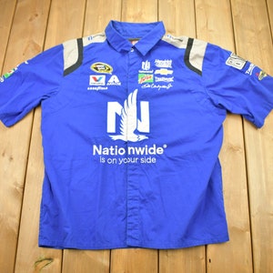 Peut inclure: Une chemise boutonnée à manches courtes bleue avec un logo Nationwide blanc et un motif d'oiseau blanc. La chemise comporte plusieurs logos de sponsors, dont Valvoline, et le texte "Nationwide is on your side".