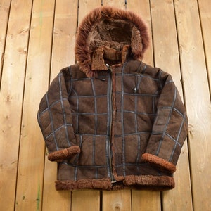 May include: A brown shearling jacket with a fur-lined hood. The jacket has a checkered pattern and a zipper closure.