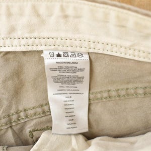 May include: Close-up of the interior of khaki-colored pants, showing the waistband, stitching, and a white tag. The tag reads "MADE IN SRI LANKA" and includes washing instructions and fabric composition details.