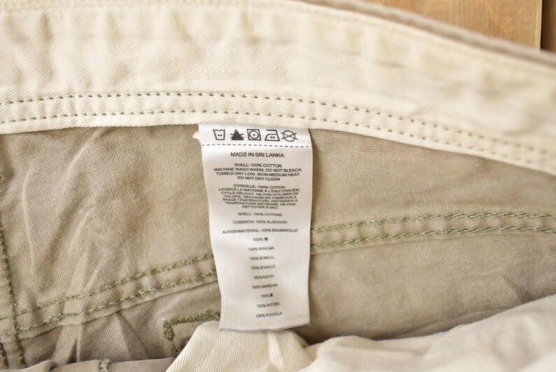 May include: Close-up of the interior of khaki-colored pants, showing the waistband, stitching, and a white tag. The tag reads "MADE IN SRI LANKA" and includes washing instructions and fabric composition details.