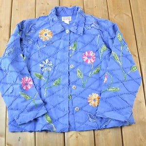 Pode incluir: Casaco azul claro com botões e flores bordadas em laranja, rosa e branco. O casaco apresenta um design acolchoado e caules e folhas bordadas em verde. A gola é de estilo clássico.