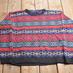 Peut inclure: Un pull coloré à motifs avec un fond noir. Le motif présente des rayures rouges, bleues, vertes et jaunes avec des motifs géométriques.