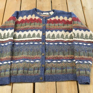 May include: A vintage blue cardigan with a button-up front. The sweater has a patterned design with red, white, green, and brown accents. It features a ribbed hem and cuffs.