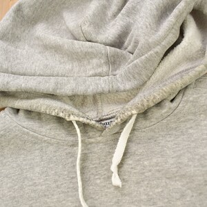 Puede incluir: Sudadera gris con capucha y cord&oacute;n blanco. La sudadera tiene una peque&ntilde;a etiqueta que dice "Champion" en el interior de la capucha.