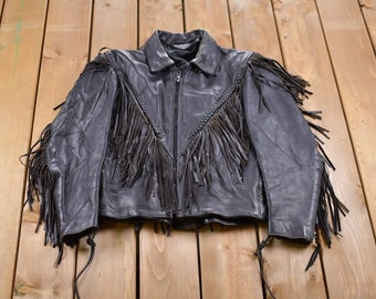 May include: A black leather jacket with fringe detailing on the shoulders, sleeves, and front. The jacket has a zipper closure and a collared neckline.