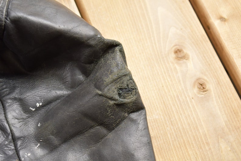 Puede incluir: Primer plano de una chaqueta de cuero negra con un parche desgastado en el codo.