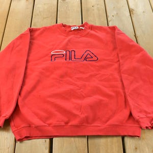 Puede incluir: Sudadera roja de FILA con el nombre de la marca bordado en blanco y azul marino en el pecho. La parte superior de cuello redondo y manga larga es de material suave.