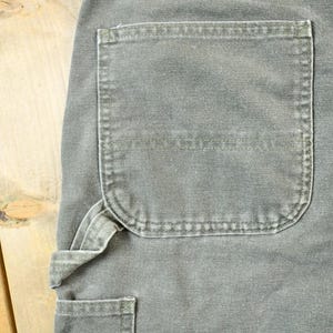 Pu&ograve; includere: Un paio di pantaloni da lavoro grigi con una grande tasca cargo sulla gamba destra. I pantaloni hanno una cintura utility e pi&ugrave; tasche.