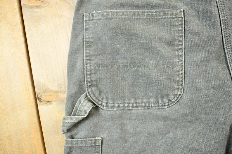Pu&ograve; includere: Un paio di pantaloni da lavoro grigi con una grande tasca cargo sulla gamba destra. I pantaloni hanno una cintura utility e pi&ugrave; tasche.