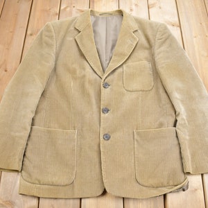 Op de afbeelding: Een beige corduroy blazer met vier knopen en twee zakken. De blazer heeft een klassieke stijl en is gemaakt van een zachte, comfortabele stof.