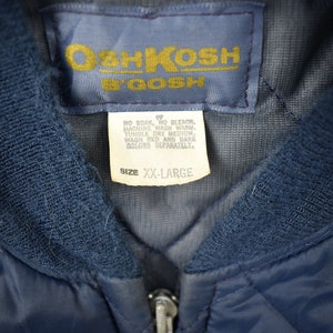 May include: A navy blue quilted jacket with a zipper closure and a label that reads "OshKosh B'Gosh" and "Size XX-Large". The label also includes care instructions.