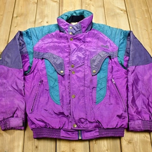 May include: A purple, teal, and blue ski jacket with a zipper closure and multiple pockets. The jacket has a quilted design and a ribbed waistband.