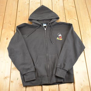 May include: A black zip-up hoodie with a hood and front pockets. The hoodie features a small embroidered image of Mickey Mouse on the left chest. The garment is made of a soft material and has a drawstring at the hood.